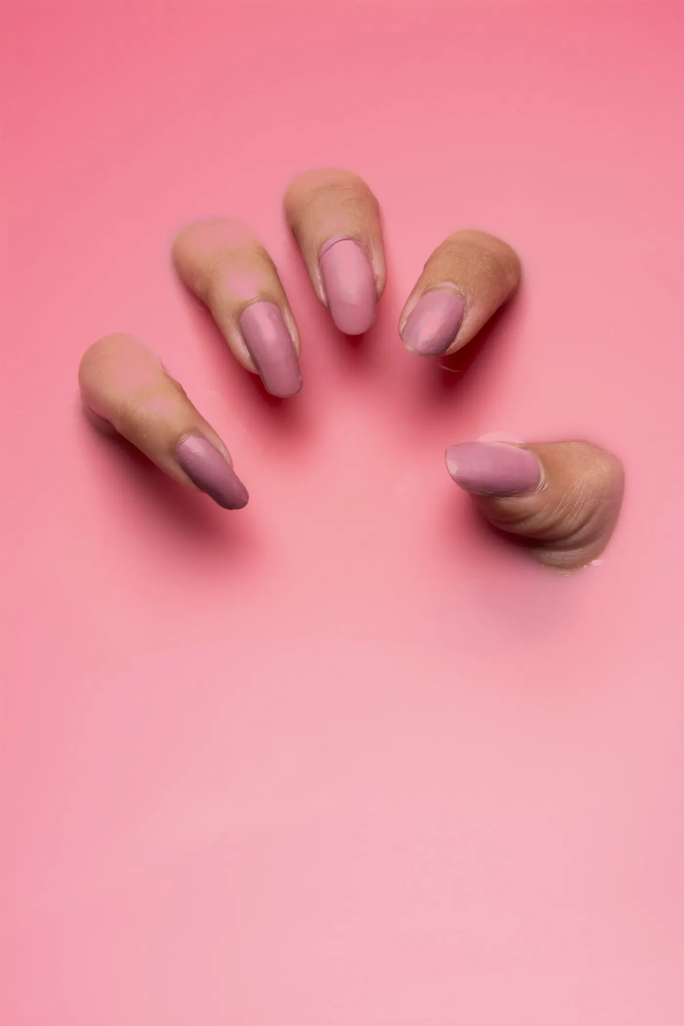Hands with nude almond nails against a pink backdrop